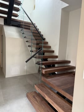 A walnut FLIGHT stair turns at a landing with frameless glass on black standoffs and a black handrail.