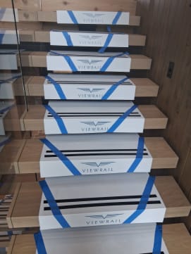 Thick white oak floating treads protected by Viewrail-branded white covers climb along a vertical wood-paneled wall.