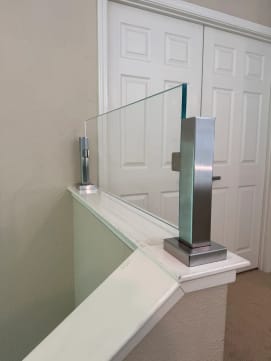 Close view of a brushed stainless post clamping a frameless glass panel atop a white knee-wall cap.