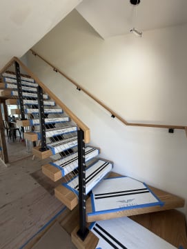 Viewrail-covered floating treads wind up beside a black-post cable railing and a wall-mounted oak handrail.