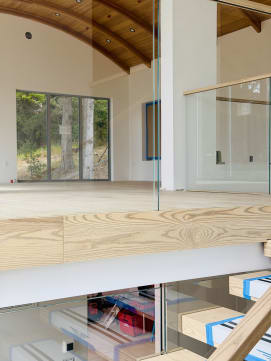 Frameless glass mounted to the face of a wood fascia lines a loft beneath a curved wood ceiling