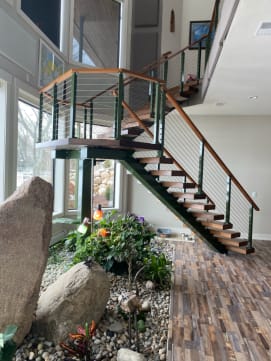 Dark stringer floating stair with wood treads and cable railing rises above an indoor rock garden.
