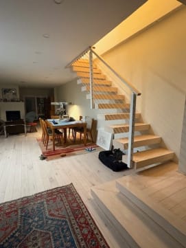 Light oak open-riser stair with a white stringer and cable railing beside a dining area.