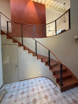 Black posts and stainless cables follow a curved cherry staircase up to a curved balcony.