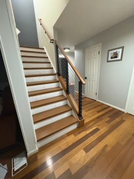 Black cable posts with a wood handrail on an angled knee wall alongside a white-riser stair.