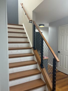 Black cable railing with a wood cap rail mounted on a knee wall beside oak treads and white risers.