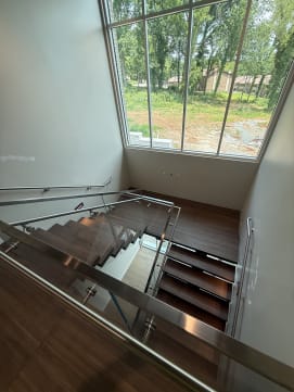 Looking down a dark wood switchback with glass and stainless handrails toward a tall window.