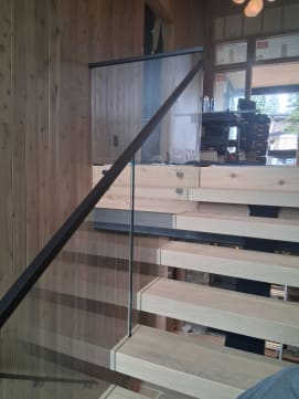 Glass railing with black handrail over floating treads