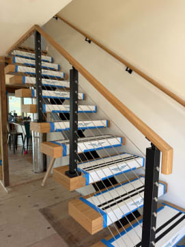 Floating stair with clean Viewrail tread covers, black cable posts and oak handrail along a white wall.
