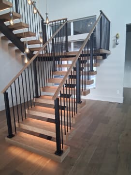 Glowing LED-lit wood treads on black mono stringers switch back at a landing with black baluster railings.