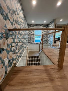 Oak newels with cable infill guarding a stair opening on a wide-plank floor.
