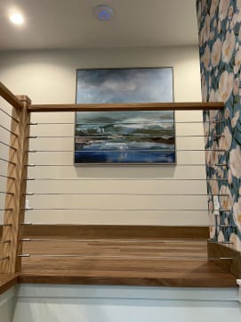 Oak newel posts and cap rail with horizontal cable infill along a landing beneath a framed seascape.