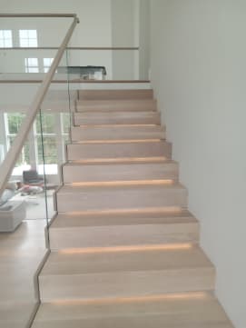 Thick white oak cantilevered treads with LED lighting beside frameless glass and a wood handrail.