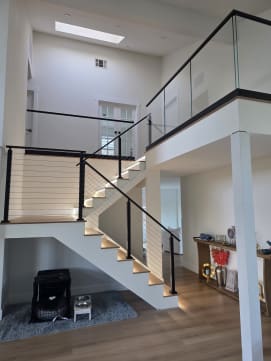 Black-post cable railing follows a white stair with LED-lit treads up to a loft guarded by frameless glass in base rail.