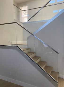 Frameless glass in a base rail with a black cap follows an angled stair wall up to a landing.