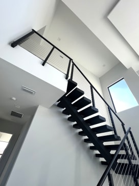 Black floating stair with black cable railing climbing a bright white double-height stairwell