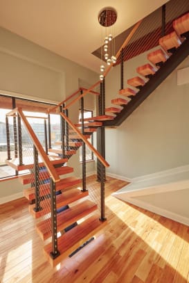Warm wood floating treads on a black stringer with cable railing and wood handrail in a sunlit stairwell.