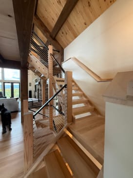 Open wood stair with square wood newels, wood handrails and cable infill in a timber-beamed great room.