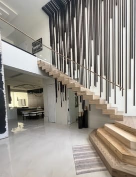 Light oak cantilevered treads rise from stacked plinth steps along a wall of black vertical slats in a glossy white foyer.