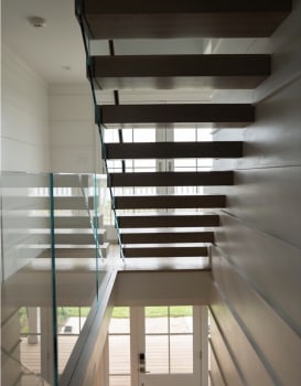White oak cantilever treads float along a paneled wall beside frameless glass