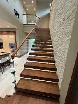 Long run of thick walnut cantilever treads along a stacked-stone wall with talon-mounted glass and wood handrail.