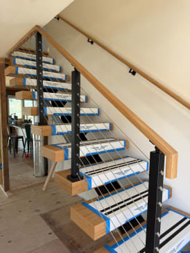 Floating stair with clean Viewrail tread covers, black cable posts and oak handrail along a white wall.