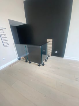 Black talon-mounted glass with a black cap rail encloses a stair opening on a pale oak floor.