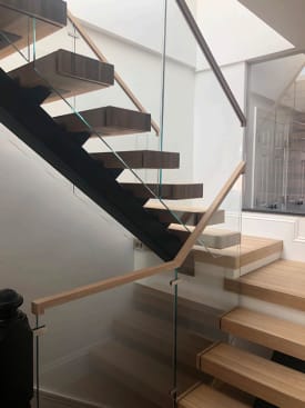 White oak floating treads on a black mono stringer with frameless glass and a light wood handrail at a switchback.