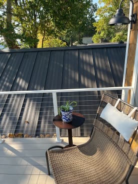 White posts and top rail with cable infill around a small composite balcony with a wicker chair.