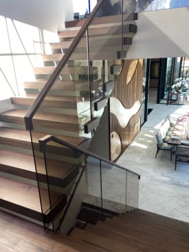 Thick-nosed walnut cantilever treads with frameless glass and a walnut handrail above a marble dining room.