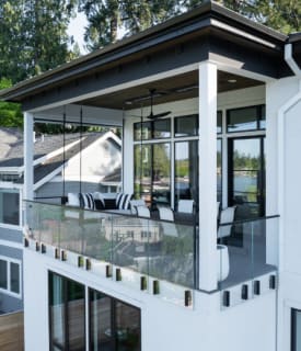 Frameless glass railing held by black side-mounted talon clamps wraps a second-story covered balcony.