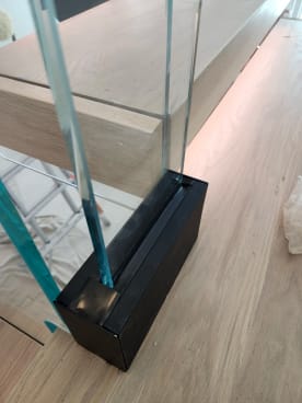 Detail of a black Vedera glass bracket holding a glass panel at the end of an oak tread