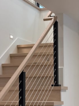 Black cable railing with white oak handrail climbing a stair of oak treads