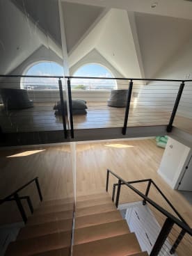 Black cable railing lines a loft beneath twin arched windows in a bright beach house