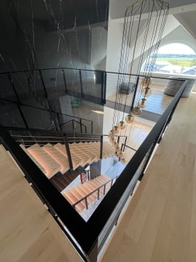Black cable railing wraps an open stairwell with LED-lit floating treads and pendant lights