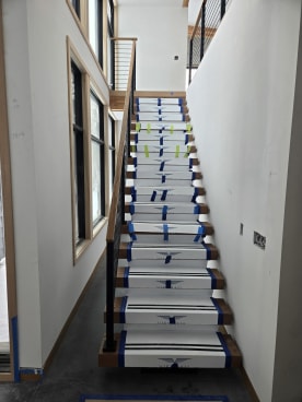 Straight floating stair in clean Viewrail tread covers with black rod railing beside tall windows