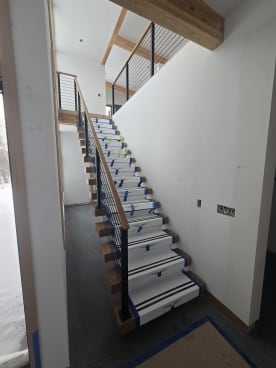 Long floating stair with black rod railing and oak handrail climbing to a loft, treads in Viewrail covers