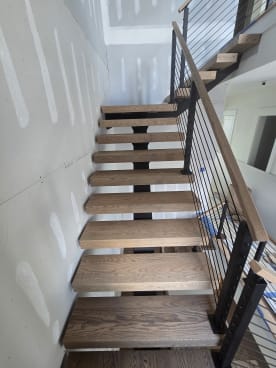 Thick red oak floating treads climbing beside black rod railing and an oak handrail