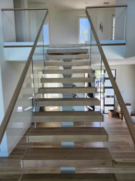 Wide white oak floating treads on a center stringer with frameless glass and oak handrails on both sides