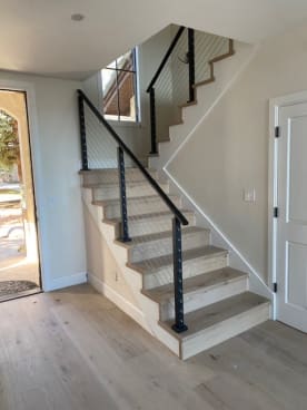 Black-post cable railing and handrail climb a white oak stair beside an arched door