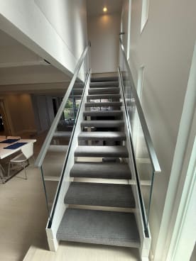 Narrow carpeted stair flanked by frameless glass in a white base rail channel with stainless handrails.