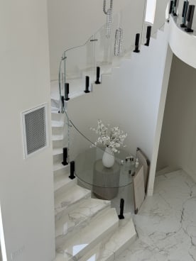 Curving white marble stair with curved frameless glass on black talons around a foyer table.