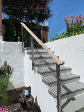 Cable railing with a wood handrail follows a bluestone stair between white stucco walls.