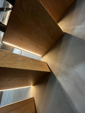 White oak cantilever treads with recessed LED strips throw dramatic light patterns on a smooth plaster wall.