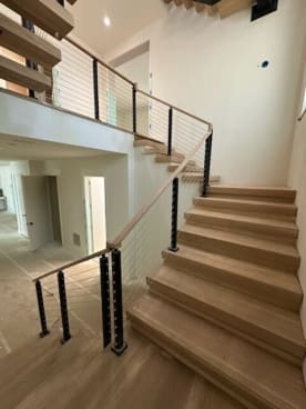 White oak treads rise to a loft lined with black cable railing and white oak cap rail in a bright white stairwell.
