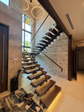 Dark wood floating treads with under-tread LEDs climb a stone wall beside glass topped with a wood cap rail.