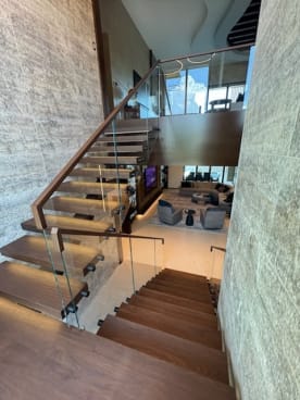 Looking down a dark wood floating stair with LED-lit treads, glass panels and a continuous wood top cap into a living room.
