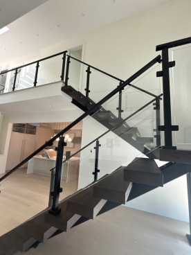 Extra-wide dark wood floating treads on black stringers with black-post glass railing in a bright modern home.