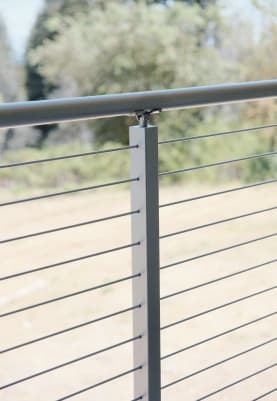 Close view of a silver cable post with round top rail and stainless cables against a field.