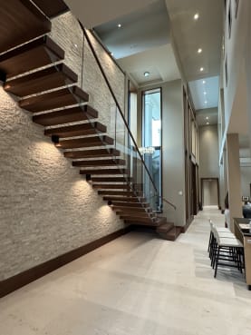 Long run of walnut floating treads along a stone wall with frameless glass and wood handrail